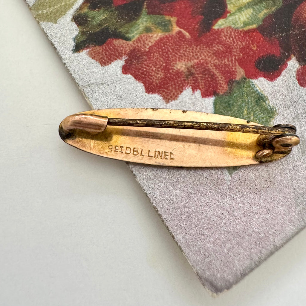 Back of antique gold lined brooch on a floral-patterned fabric background
