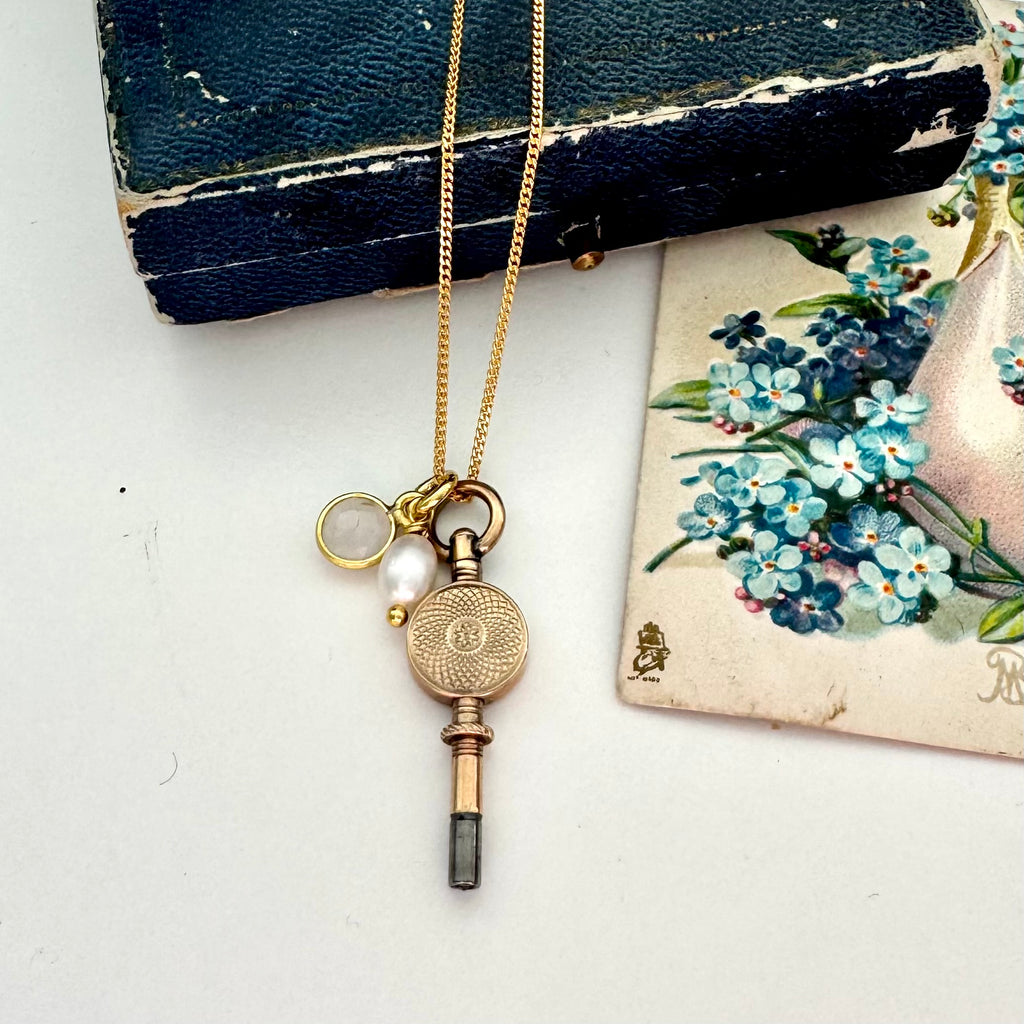 Antique 9ct gold watch key with charms and on a white background with a floral postcard and old box.