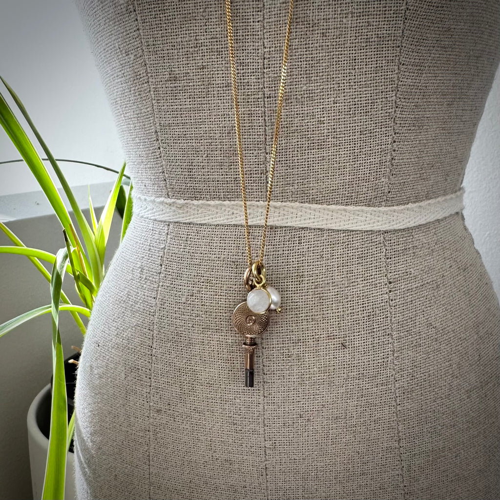 Antique 9ct gold watch key with charms on a small mannequin and with leaves in the background.