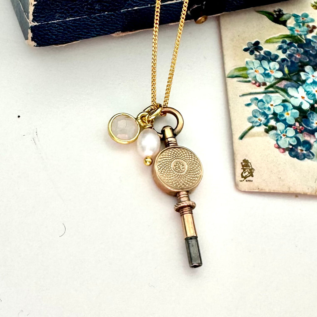 Antique 9ct gold watch key with charms and on a white background with a floral postcard and old box.