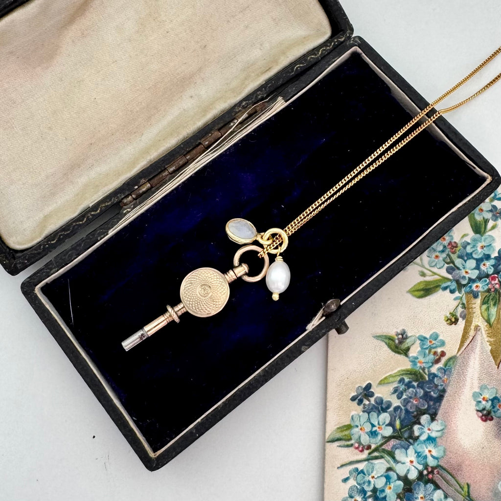 Antique 9ct gold watch key with charms and on a white background with a floral postcard and old box.