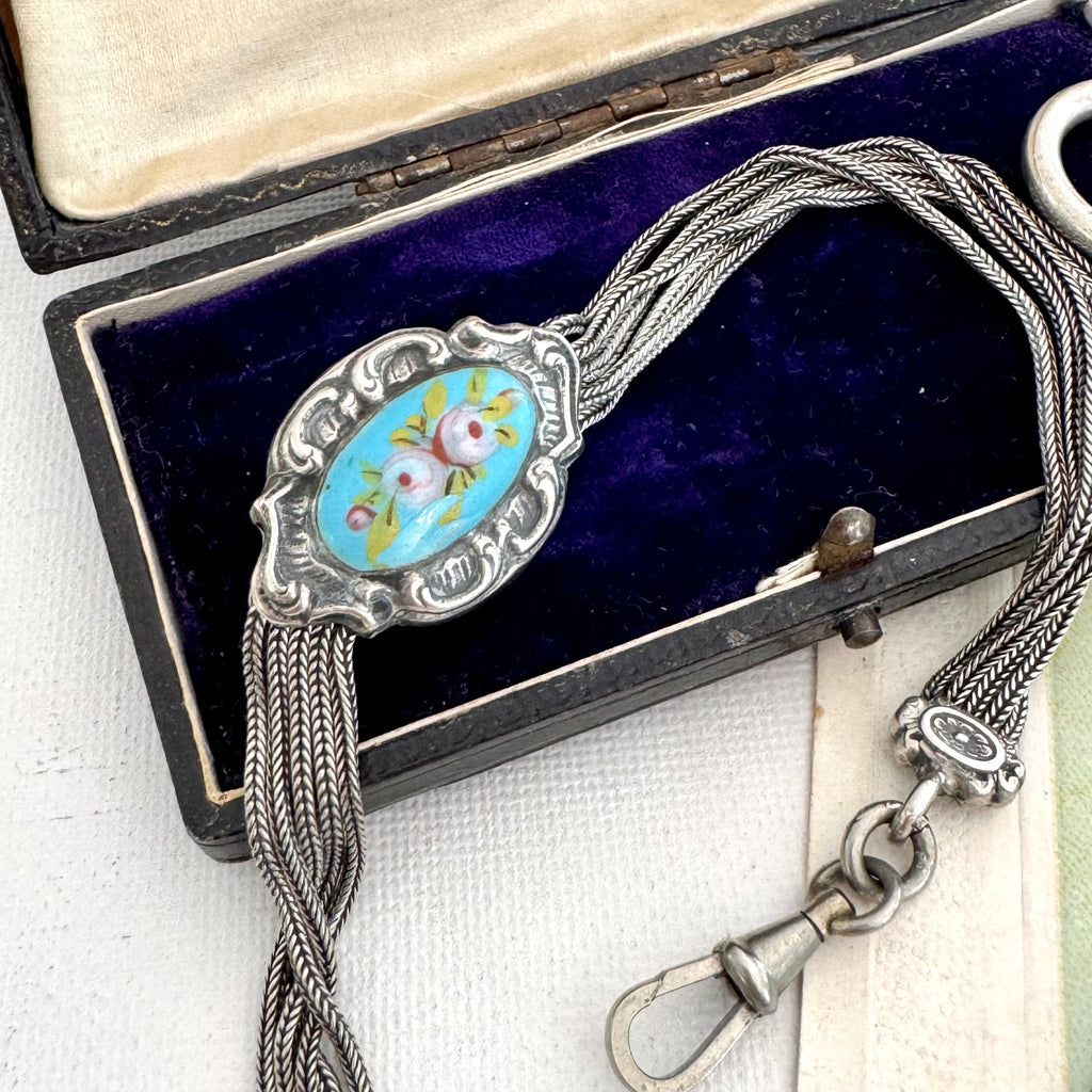 Antique French silver albertina chain with an oval enamel centerpiece, displayed inside an open dark presentation box with a purple velvet lining.
