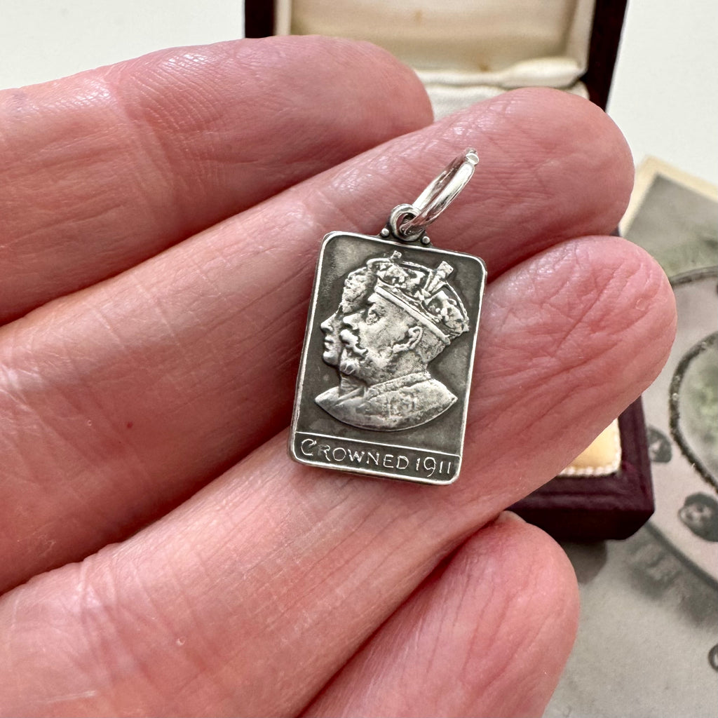 Antique silver charm commemorating the coronation of George and Queen Mary in a woman's hand