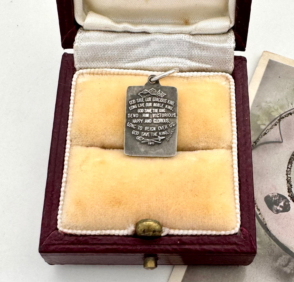 Antique silver charm commemorating the coronation of George and Queen Mary in a jewellery box. It has the words of God Save the King on the back