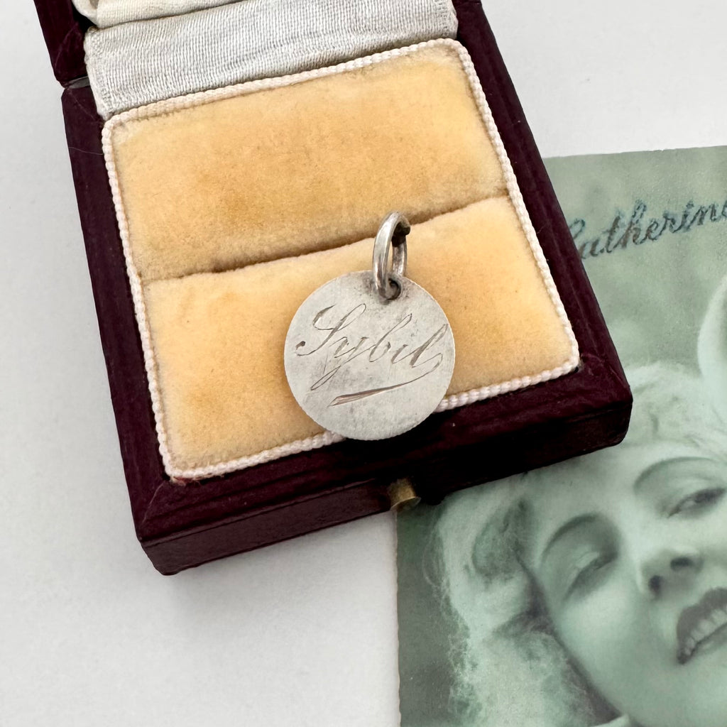 Silver pendant with engraved name in a jewelry box with a vintage photo in the background