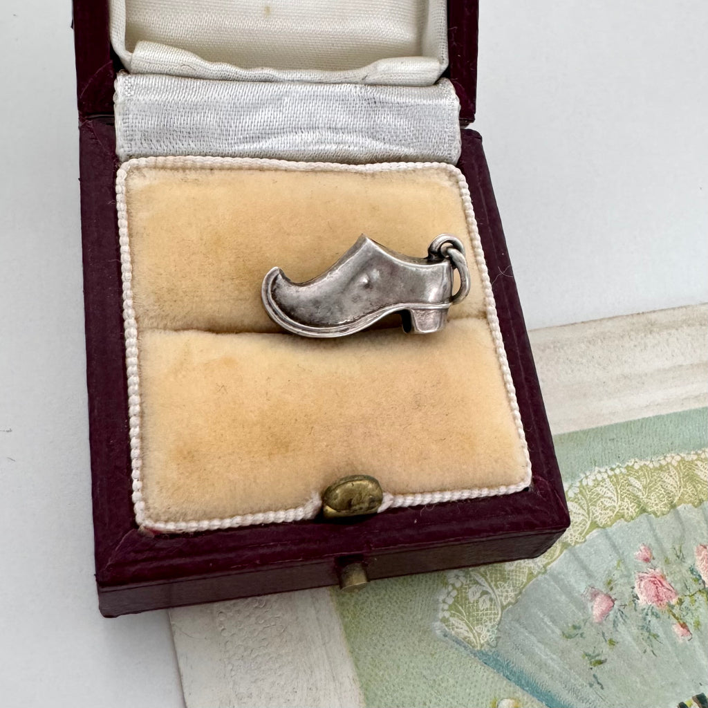 Antique silver shoe charm in a jewelry box on a textured surface