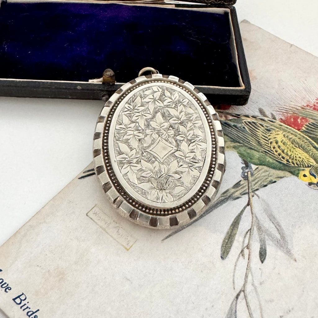 Silver lVictorian ocket with floral engraving on a vintage box with bird illustrations