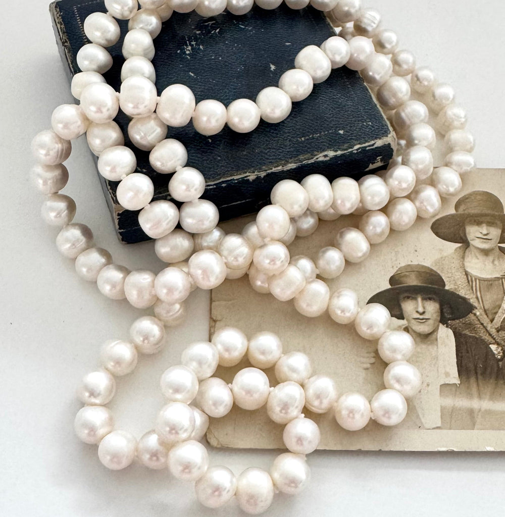 Pearl necklace on a white surface with an old photograph of two women wearing hats.
