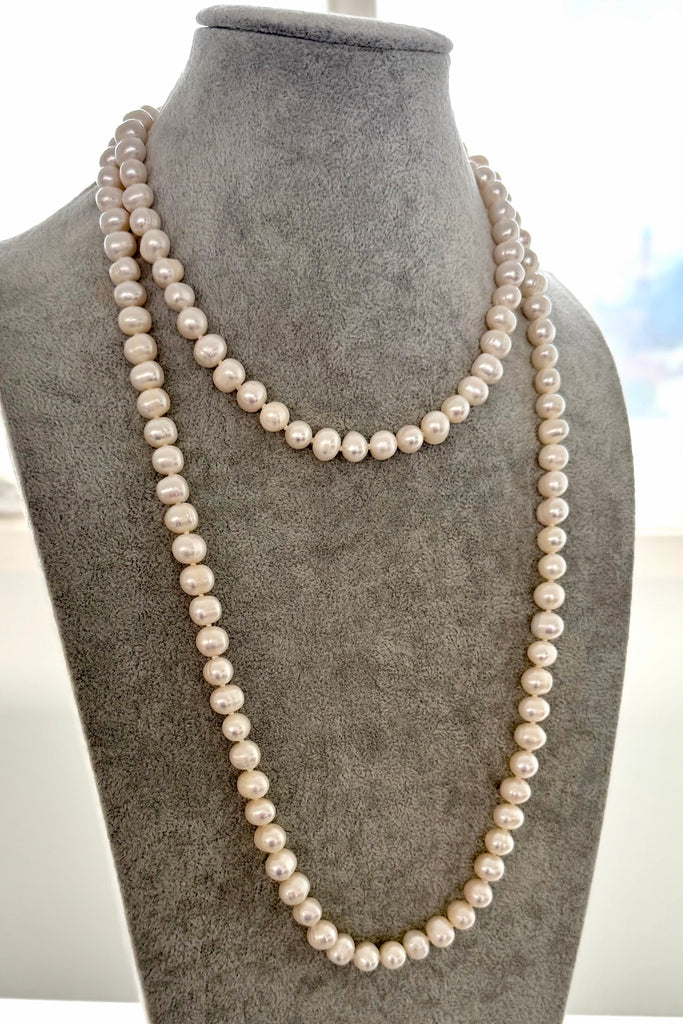 Pearl necklace on a gray mannequin bust with a blurred outdoor background