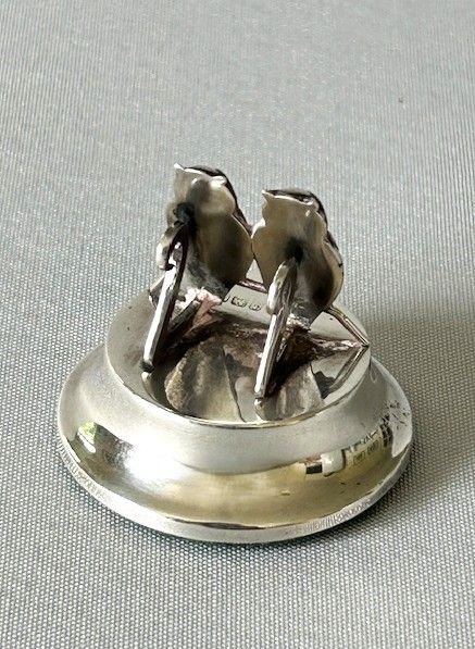 Silver menu holder with two silver earrings on a light gray background