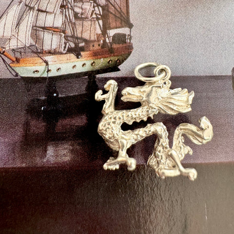 Vonk Jewellery silver Chinese dragon charm on dark background and with an image of an old sailing ship