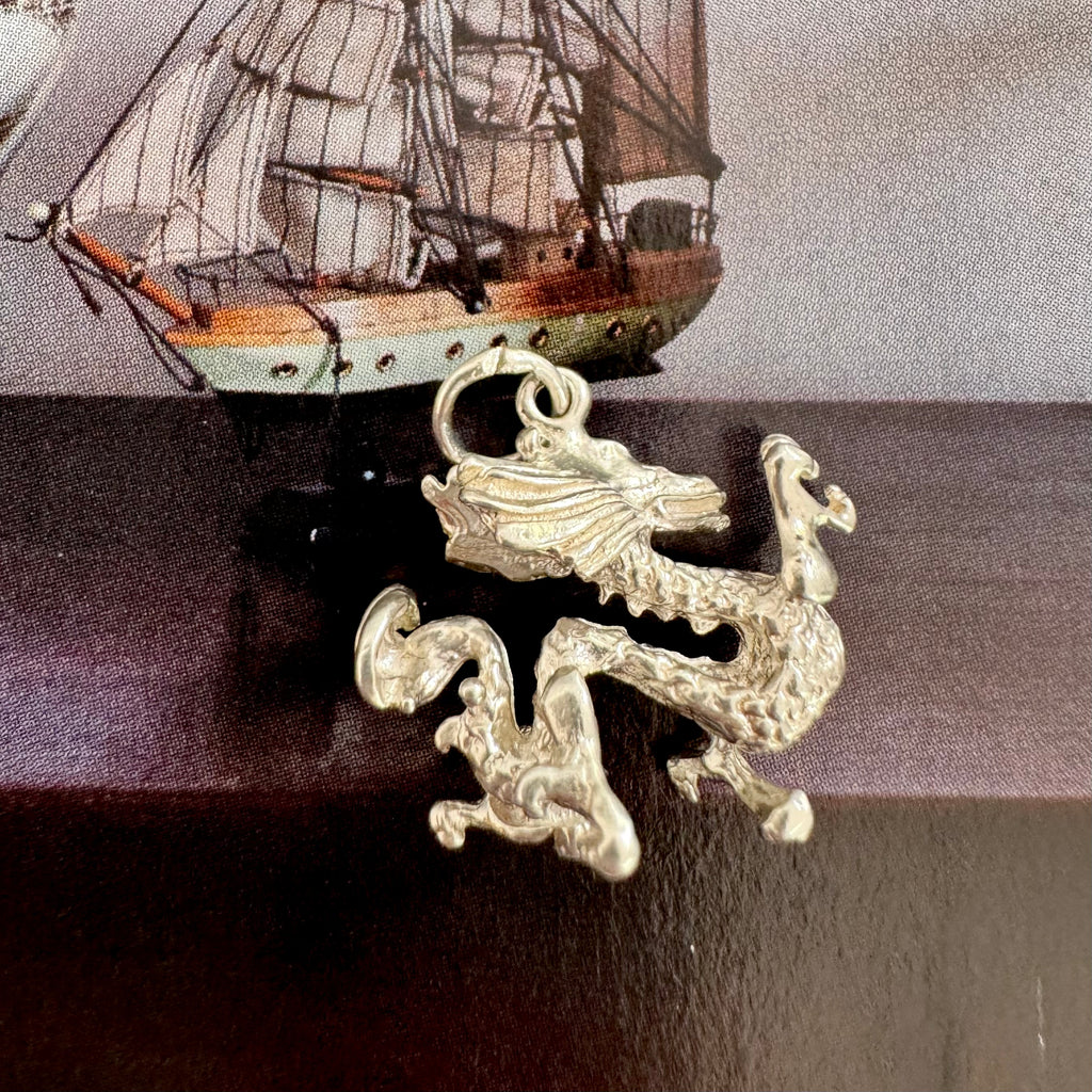 Vonk Jewellery silver Chinese dragon charm on dark background and with an image of an old sailing ship