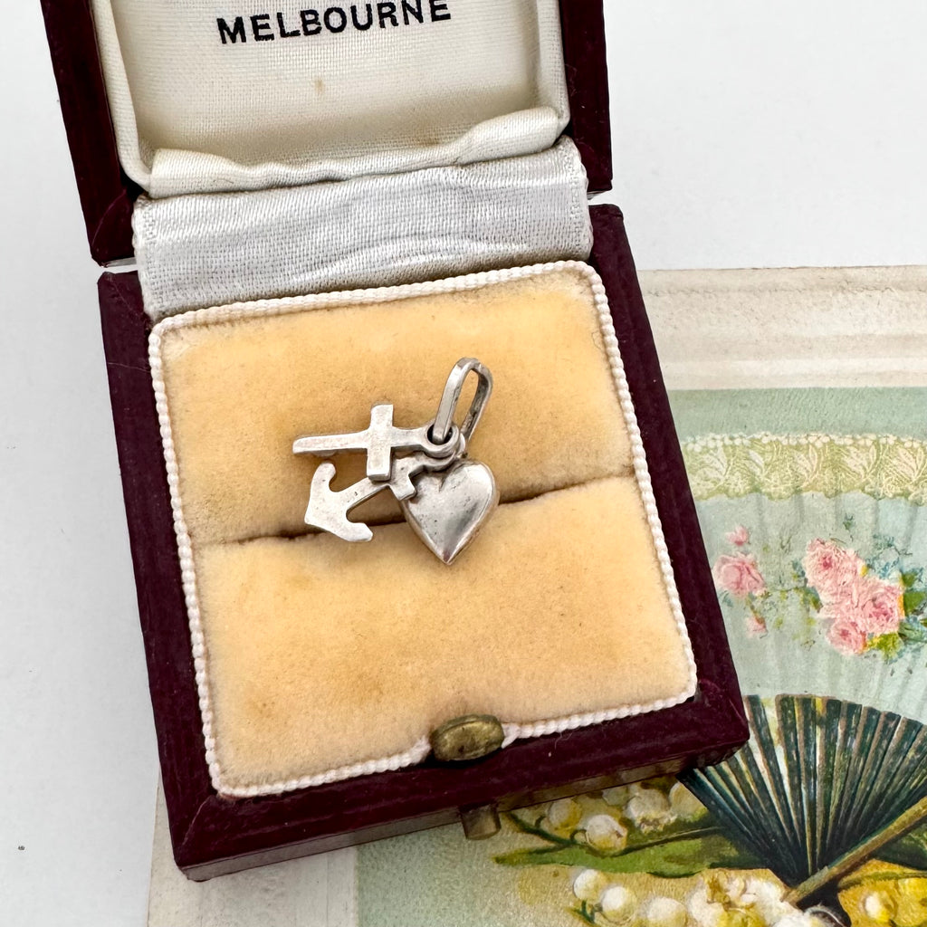 Silver faith, hope and charity charm in a jewelry box with a fan and pearls in the background