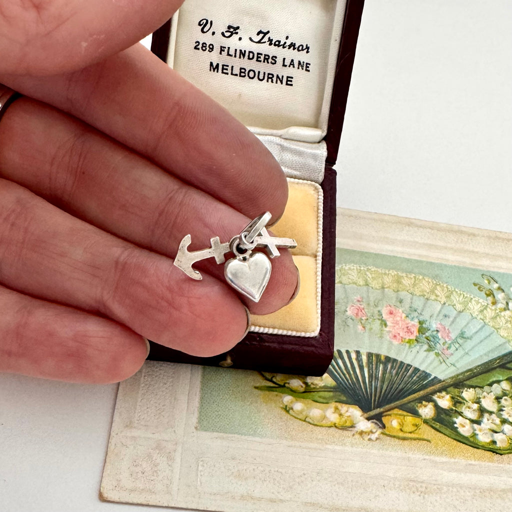 Silver faith, hope and charity charm held by a hand with an antique box and fan in the background.