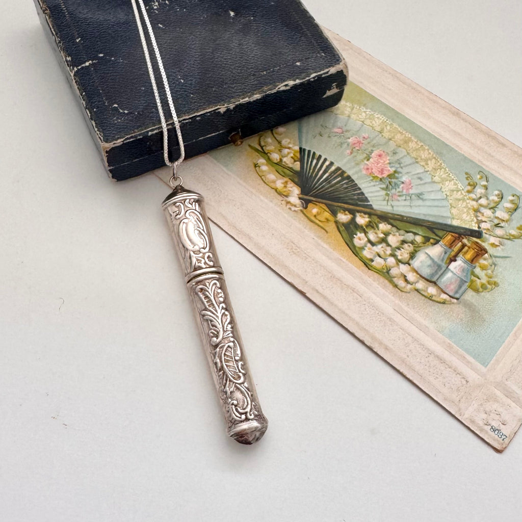 Vintage silver needle case on a white surface with an old book and vintage-style illustration.