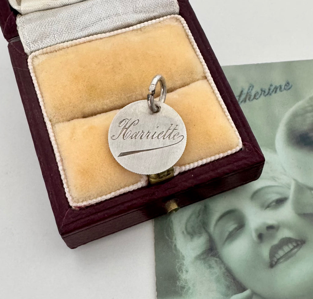 Silver pendant with engraved name in a velvet box, with a vintage photo in the background.
