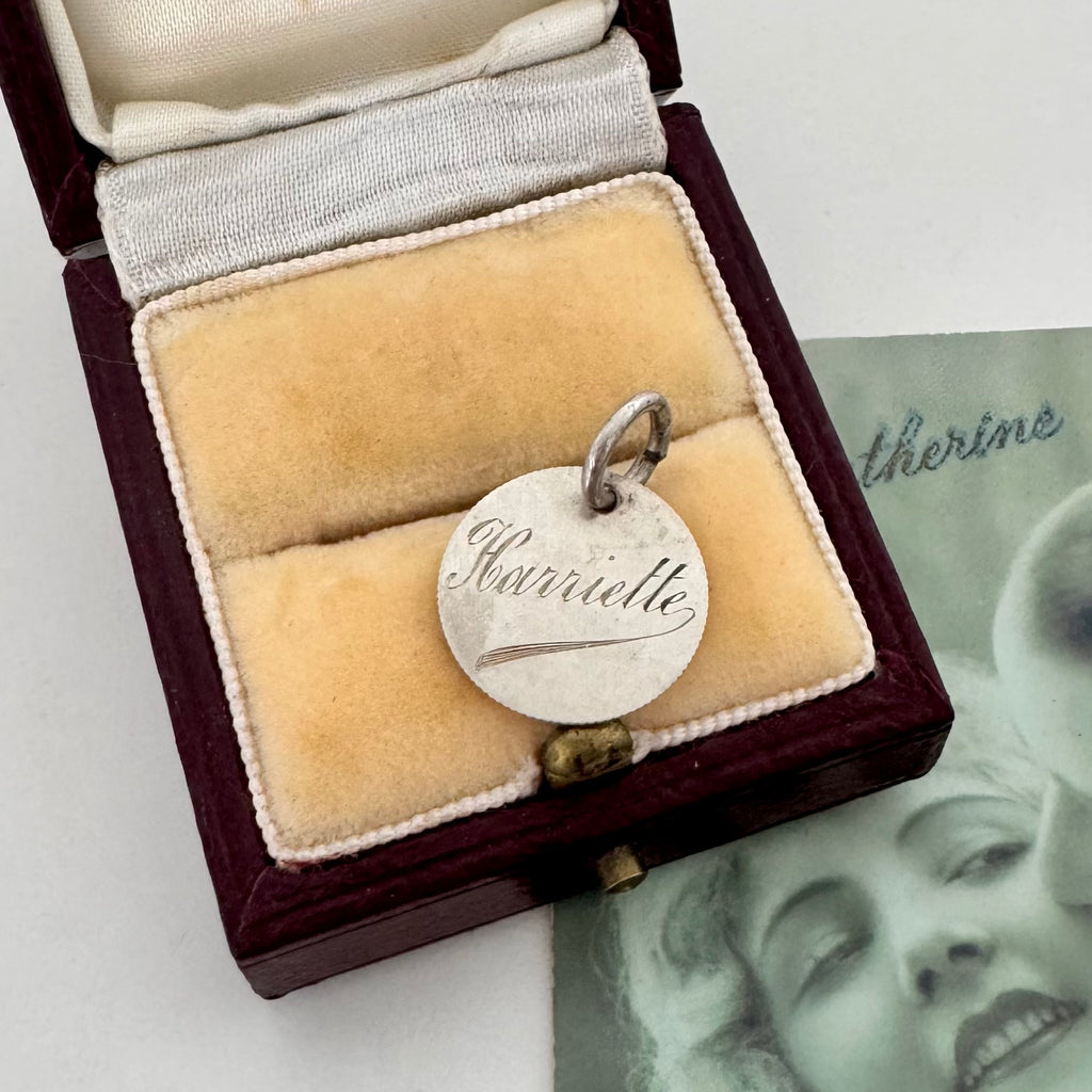 Silver pendant with 'Harriette engraved on a beige cloth inside an open jewelry box.