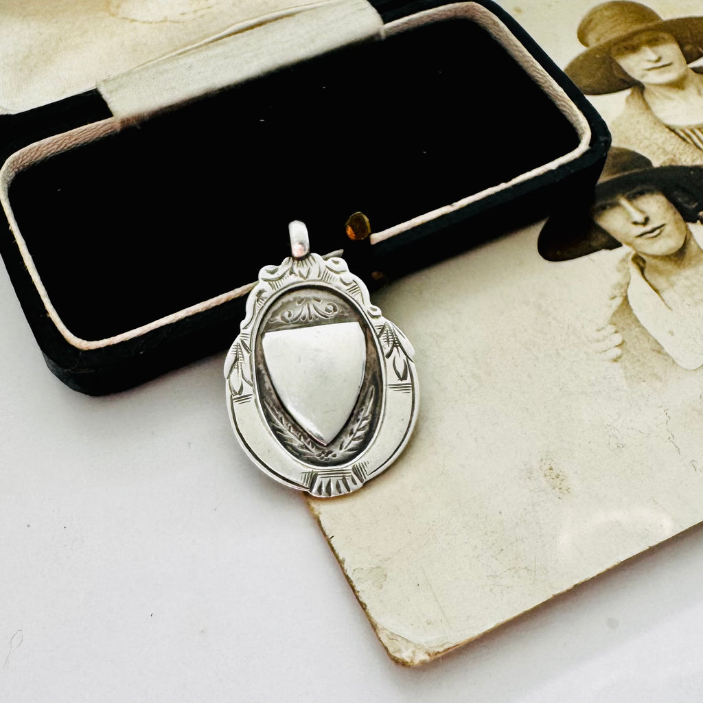 Vintage 1932 Fattorini sterling silver 1932 watch fob pendant with ornate detailing, displayed on top of an antique sepia-toned photograph and a black jewelry box.