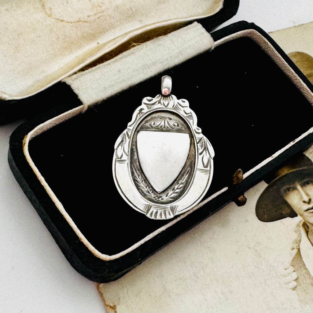 Vintage 1932 Fattorini sterling silver 1932 watch fob pendant with ornate detailing, displayed on top of an antique sepia-toned photograph and a black jewelry box.