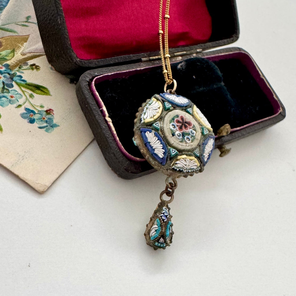 Decorative micro mosaic pendant necklace in an open jewelry box on a white surface