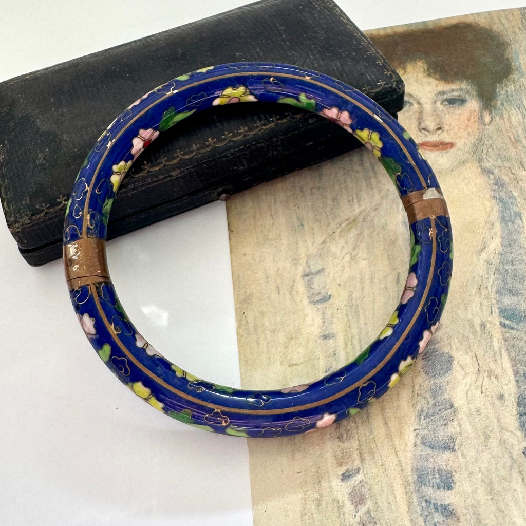 Decorative blue cloisonne bangle with floral patterns on a textured surface