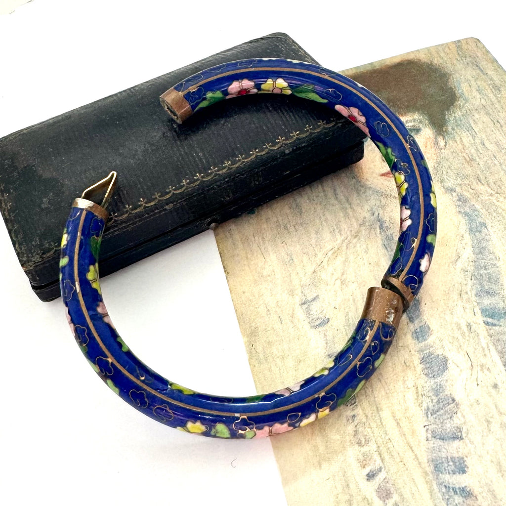 Blue cloisonne floral-patterned bracelet on a textured surface with a black box.