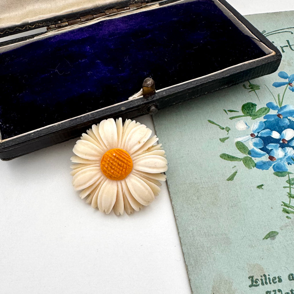 Vintage Danish hand carved daisy shaped brooch on a floral-patterned card with an open jewelry box.