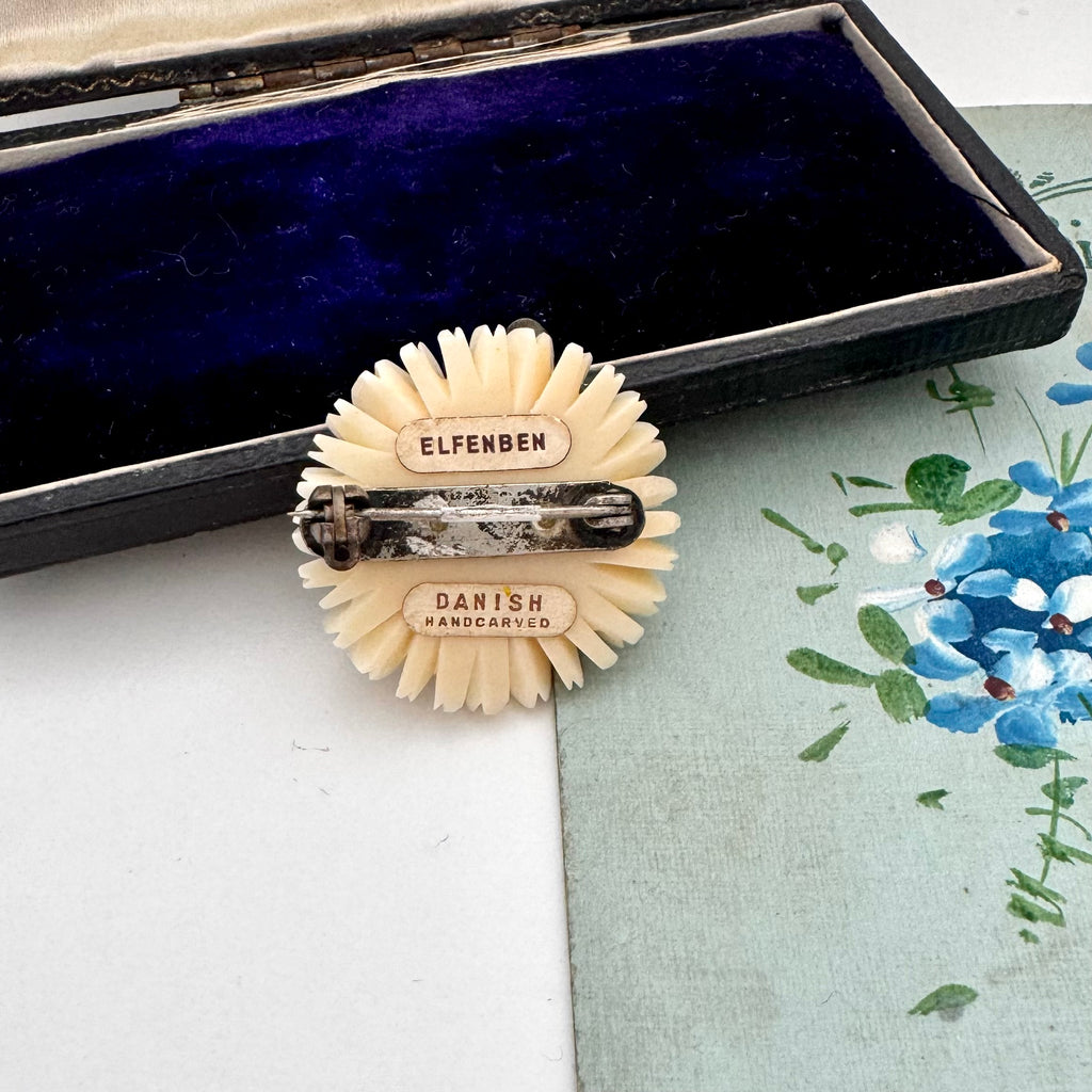 Decorative vintage daisy brooch with 'Elfenben' and 'Danish Handcarved' labels on a floral background