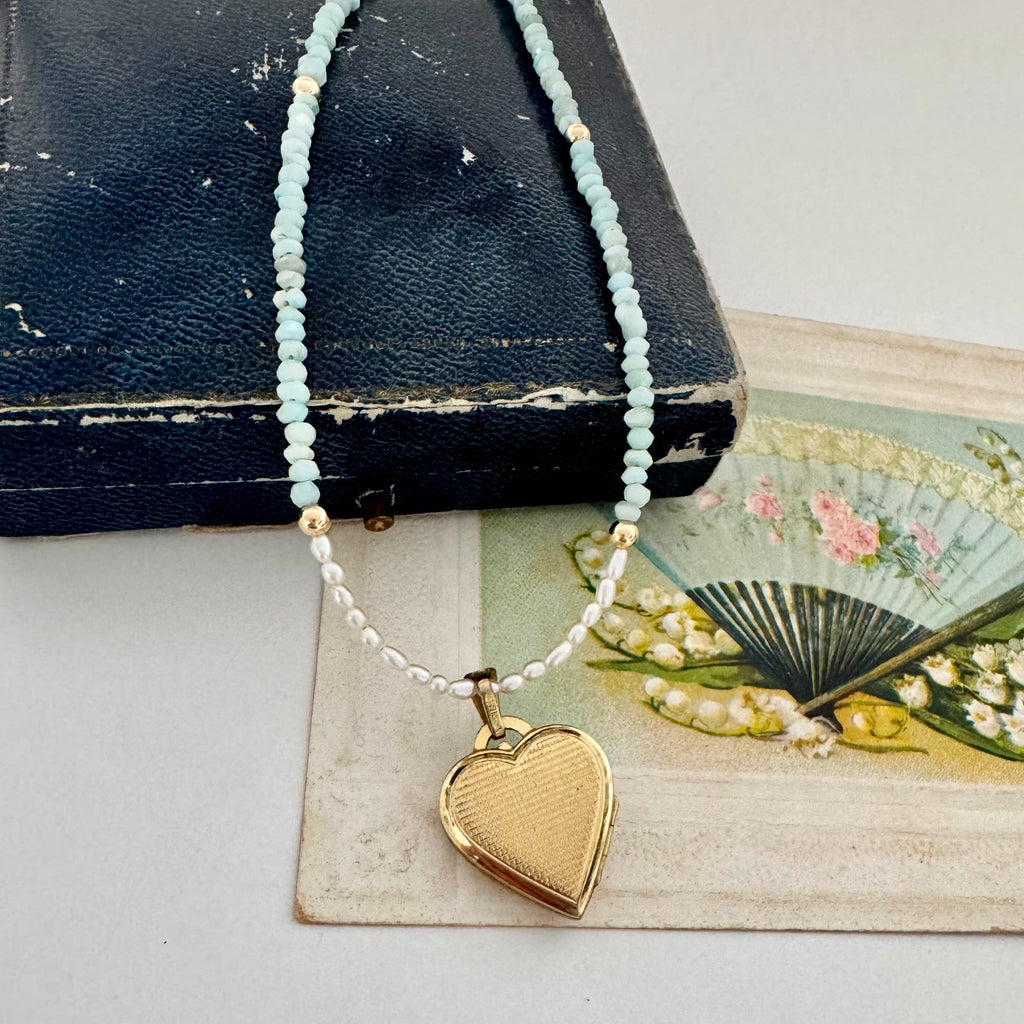 Pearl and larimar necklace with a vintage heart-shaped mother of pearl and gold locket on an old box and fan illustration