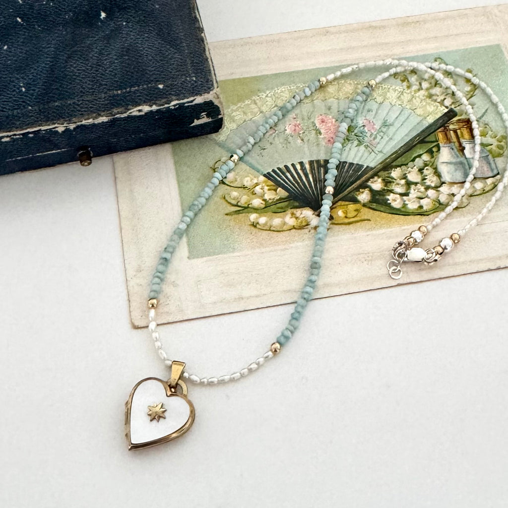 Pearl and larimar necklace with a vintage heart-shaped mother of pearl and gold locket on an old box and fan illustration