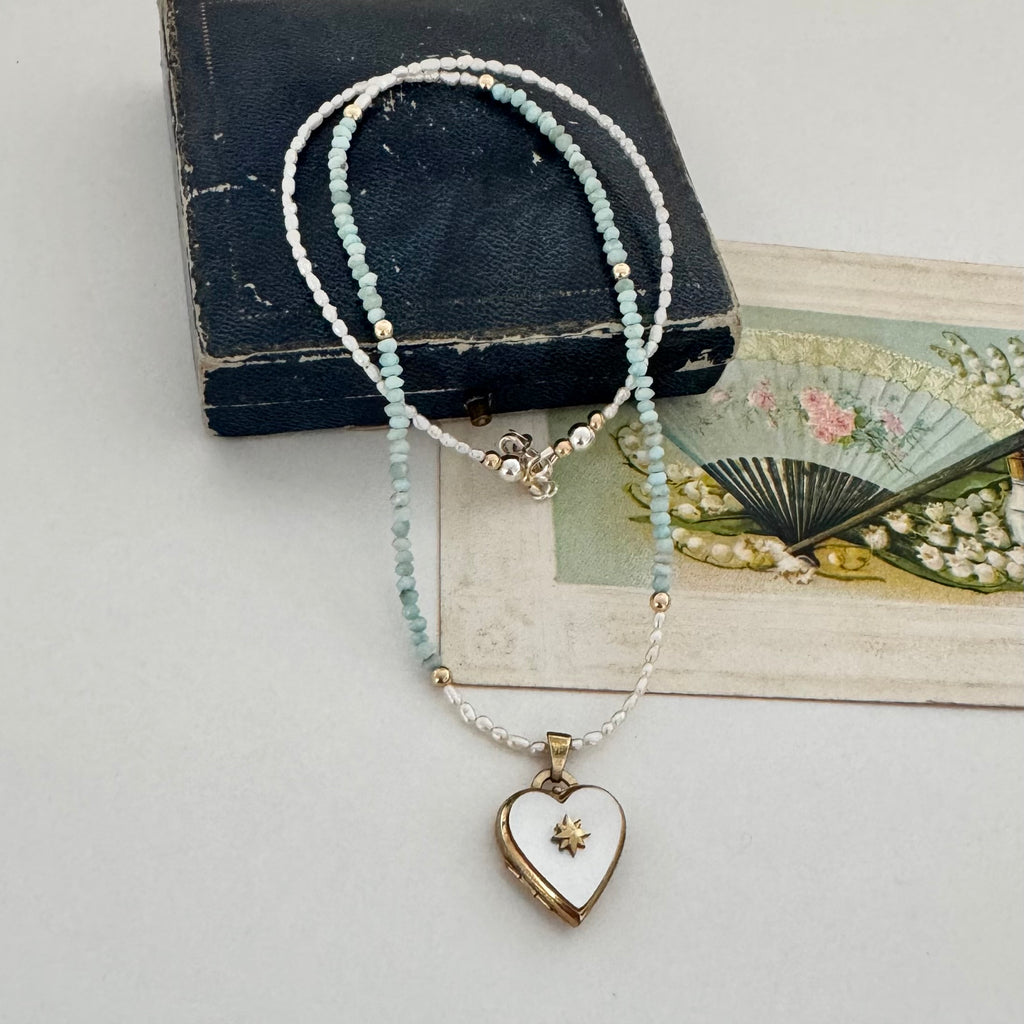 Pearl and larimar necklace with a vintage heart-shaped mother of pearl and gold locket on an old box and fan illustration
