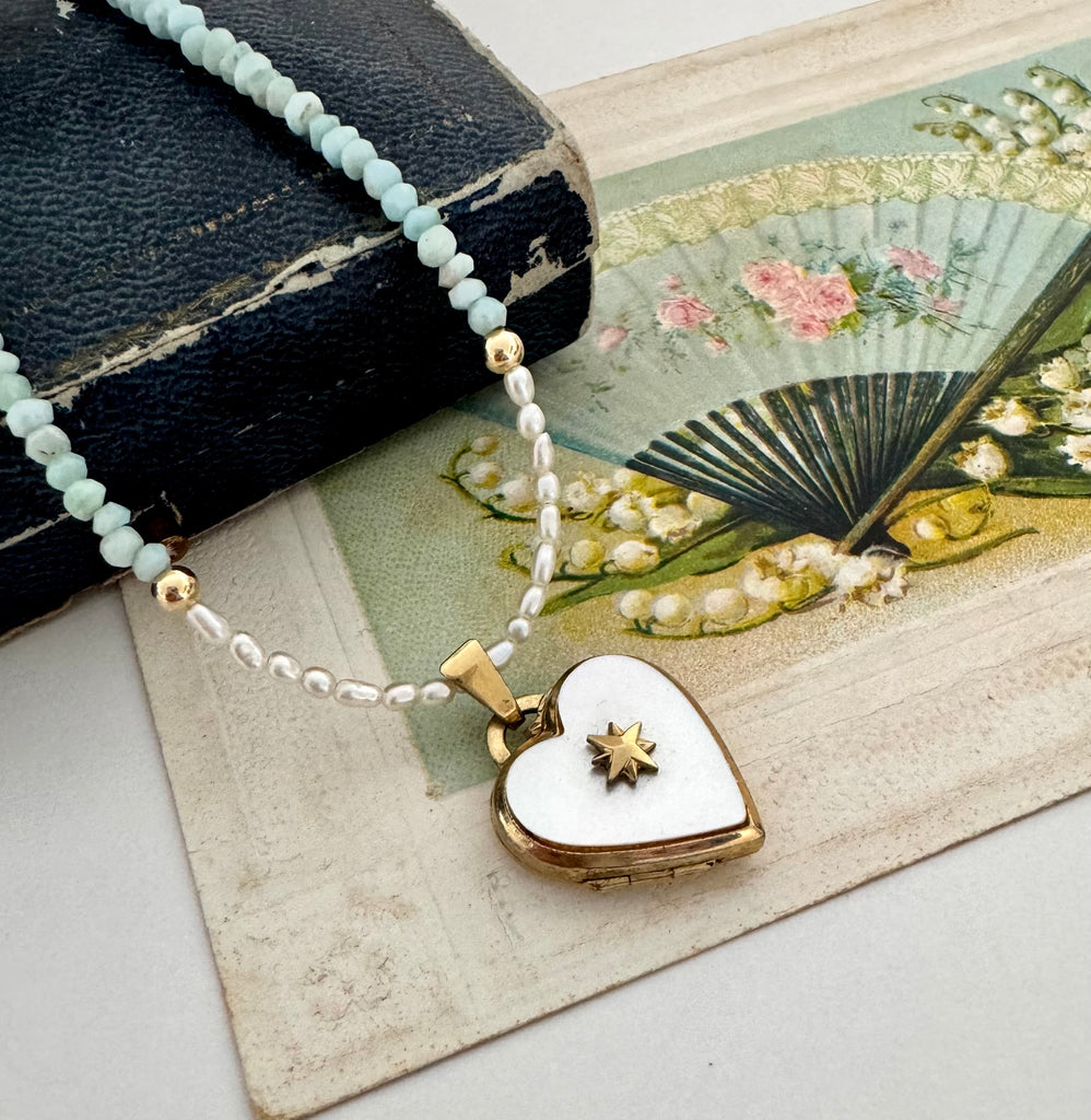 Pearl and larimar necklace with a vintage heart-shaped mother of pearl and gold locket on an old box and fan illustration