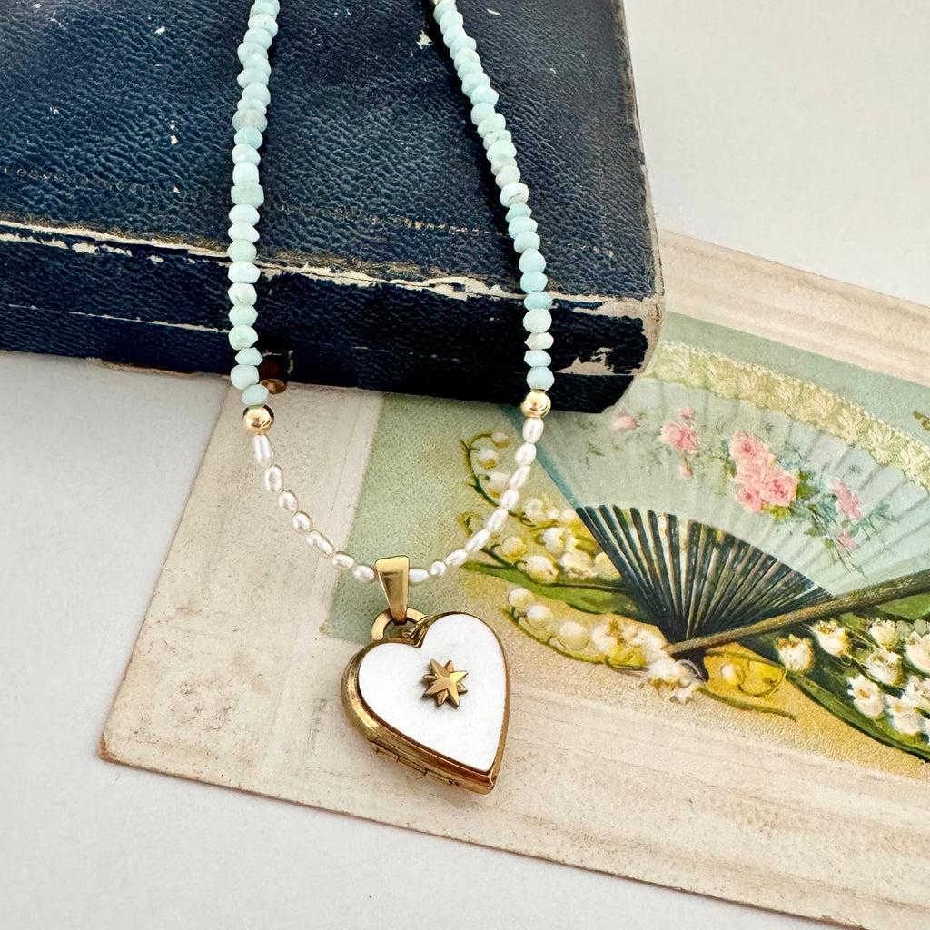 Pearl and larimar necklace with a vintage heart-shaped mother of pearl and gold locket on an old box and fan illustration