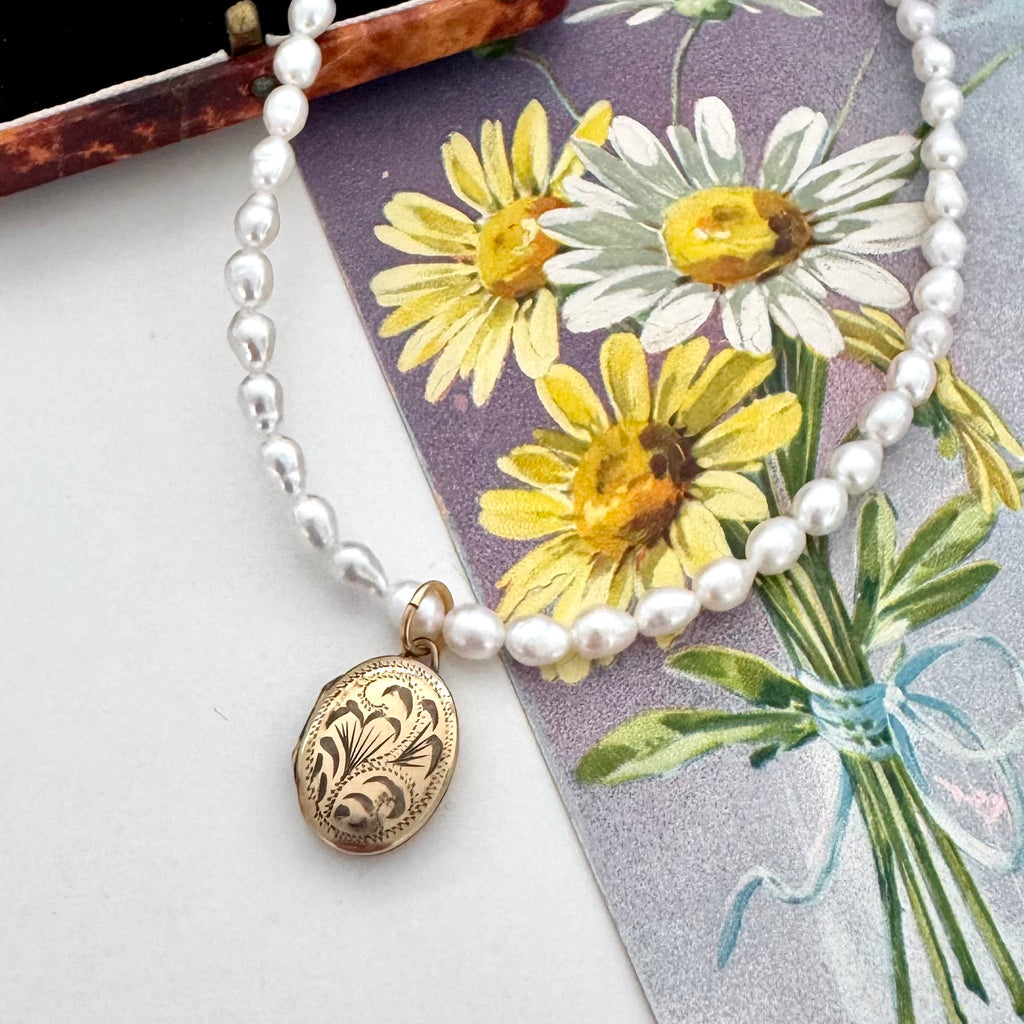 A white pearl beaded necklace with an oval rolled gold engraved vintage locket, displayed diagonally over a vintage floral card featuring yellow daisies.