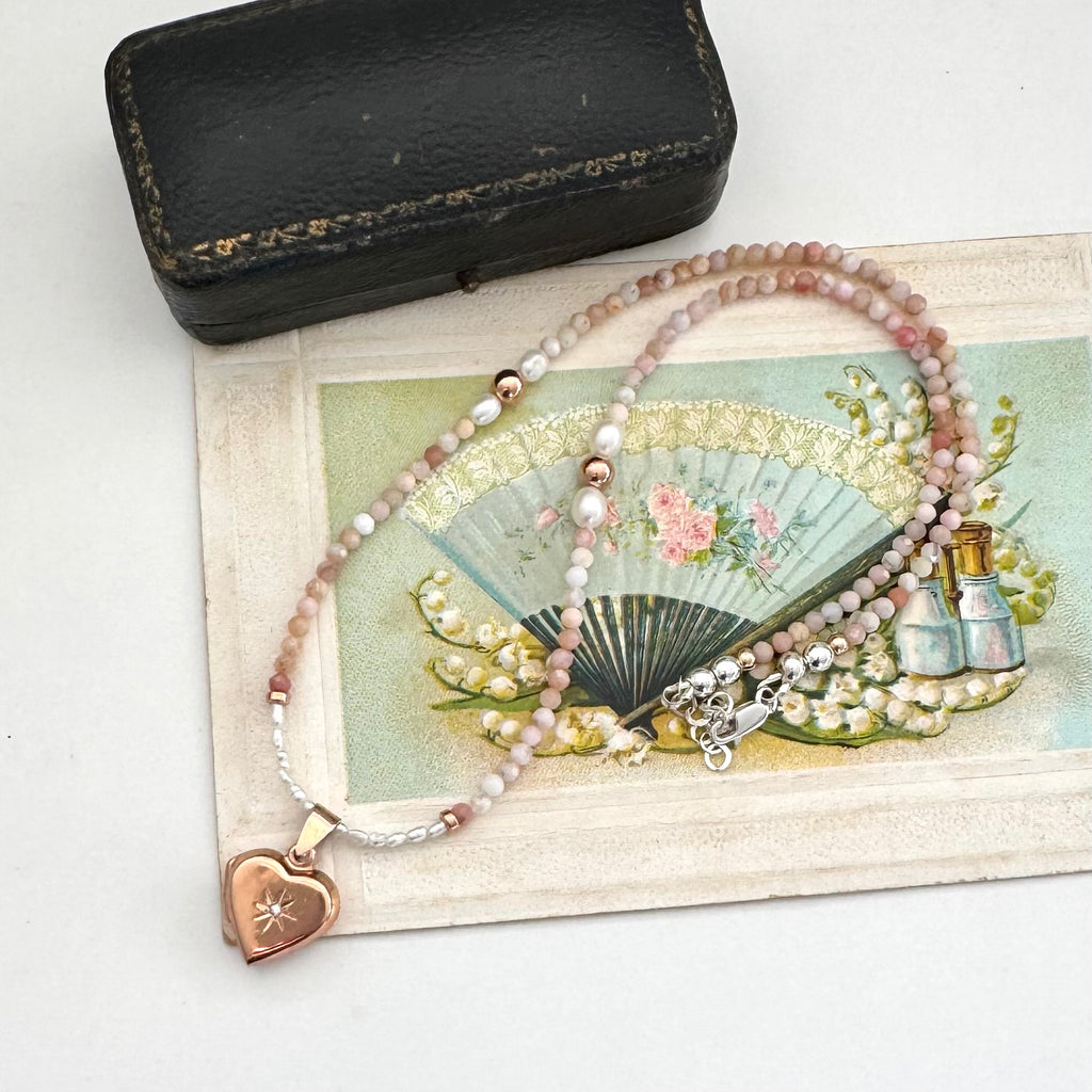 Peruvian opal and pearl necklace with heart locket on a vintage-style card with fan and bottle illustration