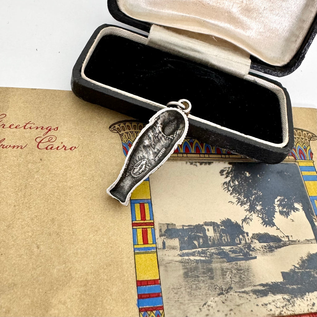 Silver pendant with a detailed design on a vintage card with Egyptian-themed border