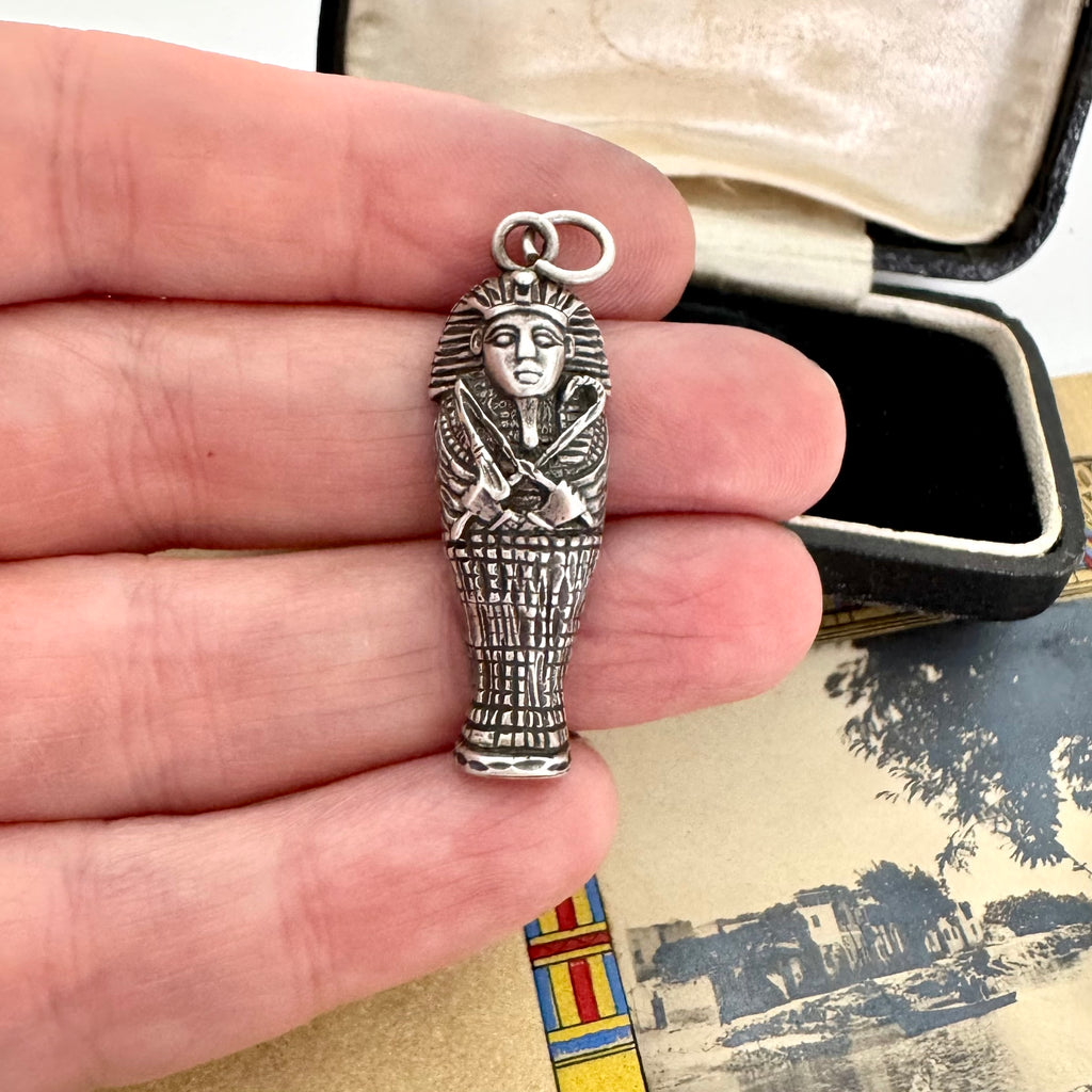 Silver sarcophagus pendant held between fingers with a vintage-style background