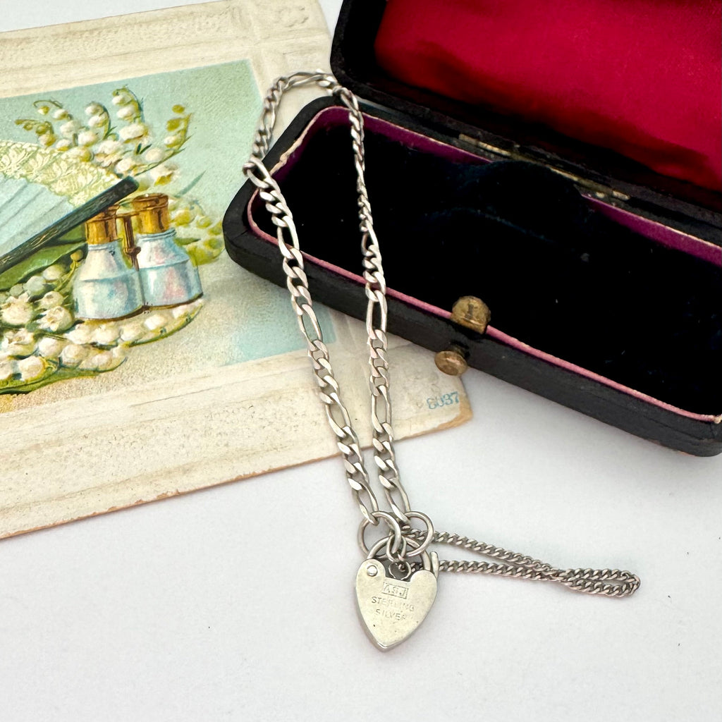 Silver chain necklace with heart-shaped tag on a white surface next to an open jewelry box.
