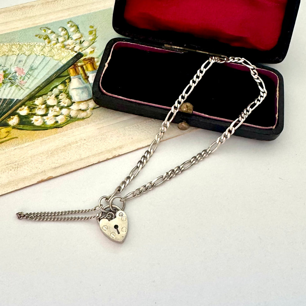 Silver chain necklace with a heart-shaped lock pendant on a white surface.