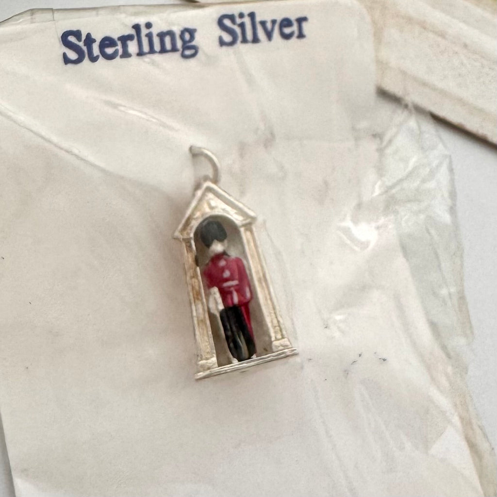 A miniature sterling silver pendant shaped like a guardhouse with a tiny figure inside wearing a red uniform, displayed on its white backing card labeled 'Sterling Silver'.