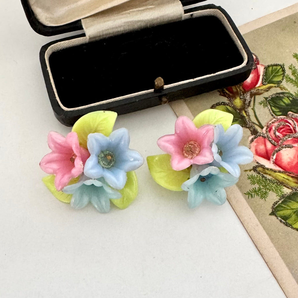 Pair of vintage floral earrings with pastel colors on a white surface.