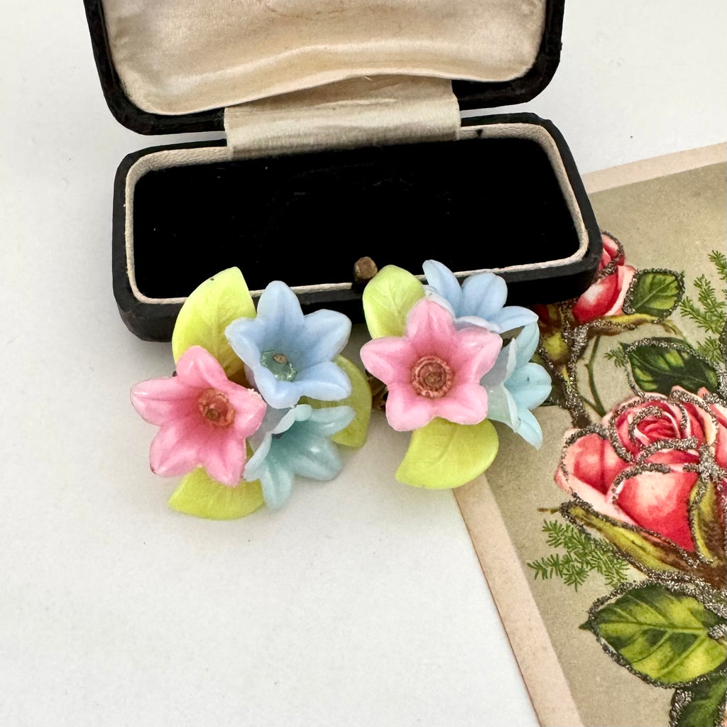 Vintage floral earrings in an open black jewelry box on a white surface with a floral-themed card.