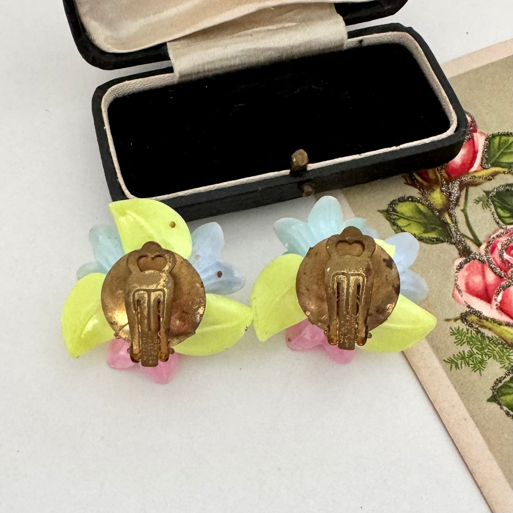 Back of vintage clip on earrings on a white background with an old jewellery box and postcard.