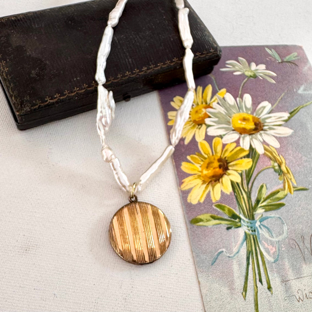 Necklace with pearls and a vintage gold locket on a textured surface with floral card