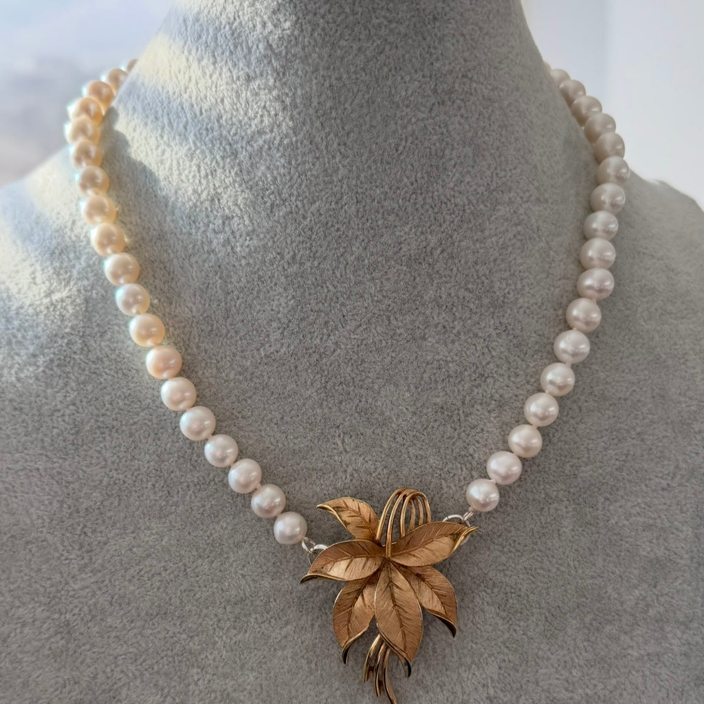 A pearl necklace with a gold-toned flower pendant, displayed on a gray jewelry bust.