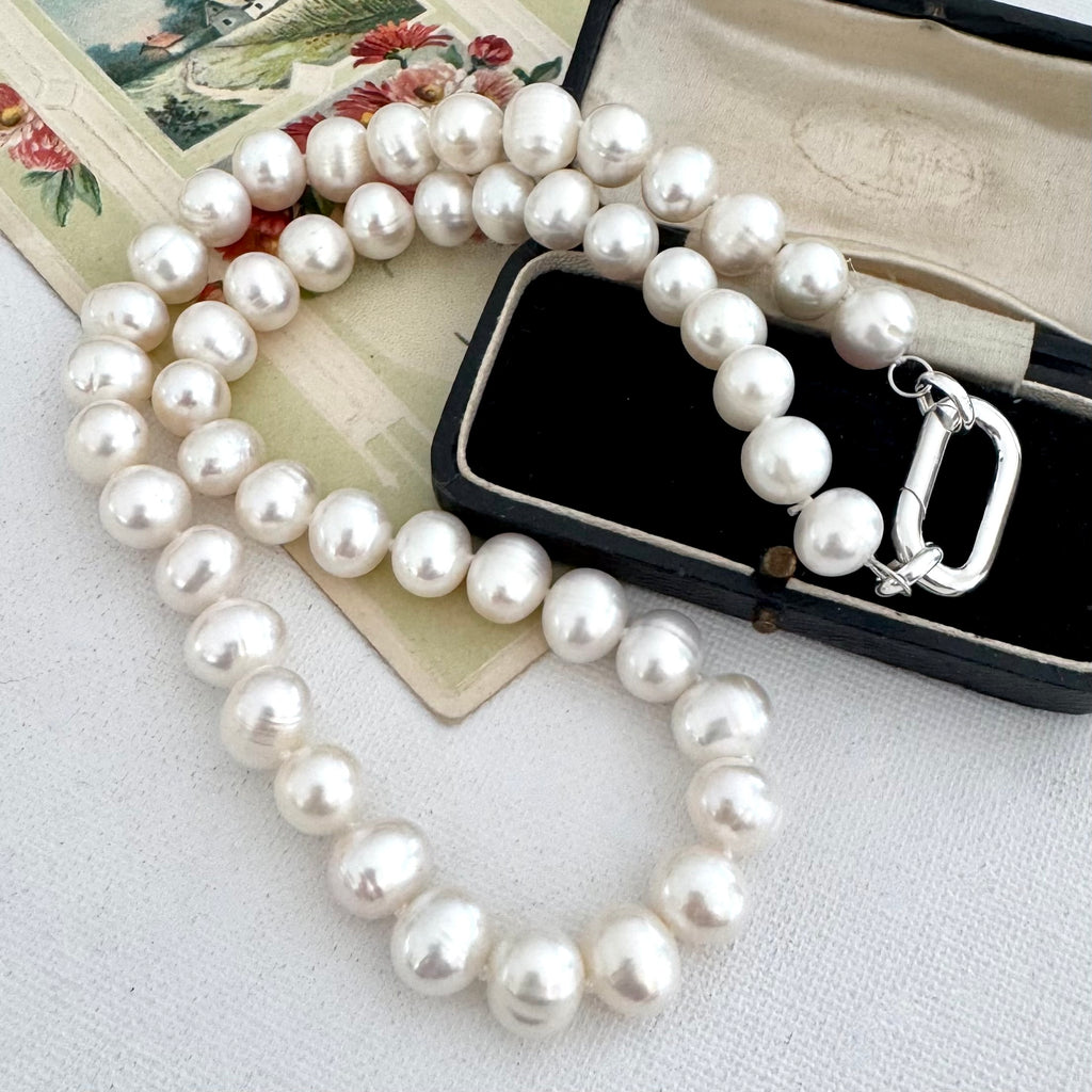 A pearl necklace with a silver clasp, displayed on a vintage floral card and a black jewelry box.