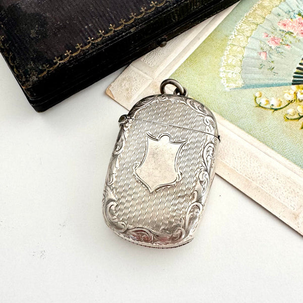 Antique 1876 silver vesta case pendant on a white background and with a vintage postcard and old box