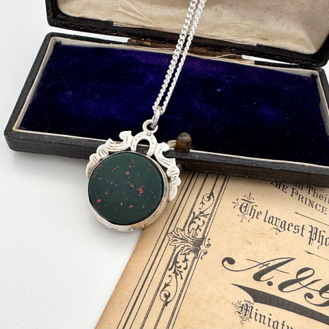 Antique 1905 watch fob necklace with a dark green stone in a silver setting on an open book