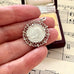 Silver pendant with a coin insert held between fingers on sheet music