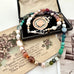 Vonk Jewellery 1927 watch fob and pearl, crystal and gemstone necklace on a vintage jewellery box and vintage postcards.